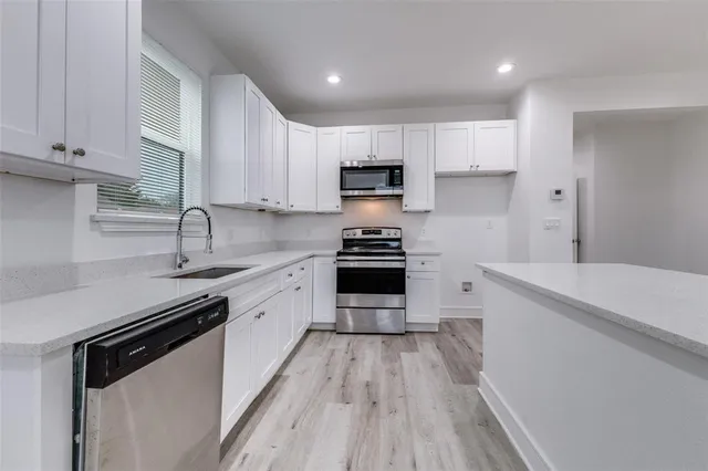 a kitchen with granite countertop a sink dishwasher stove and white cabinets with wooden floor