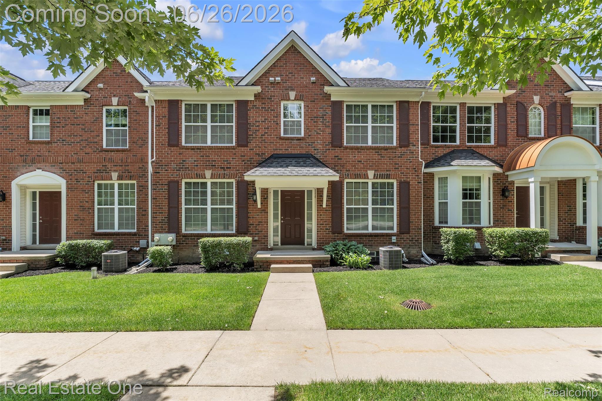 41590 Mitchell Road Novi, MI 48377 - Photo 2 of 45 Brick townhouse facade featuring white-framed windows with dark shutters, covered entryways, a bay window, a copper-clad awning, and a manicured lawn with a concrete walkway