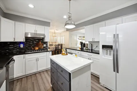 a kitchen with a refrigerator a stove a sink and white cabinets with wooden floor