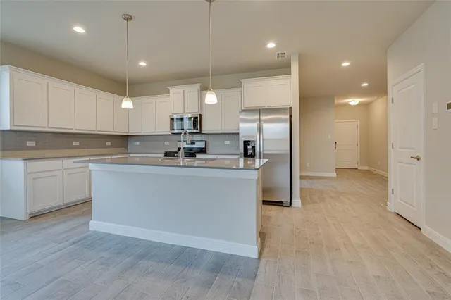 a kitchen with stainless steel appliances granite countertop a refrigerator a sink a stove and white cabinets with wooden floor