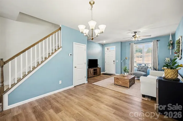 a living room with couches chandelier and a dining table with wooden floor