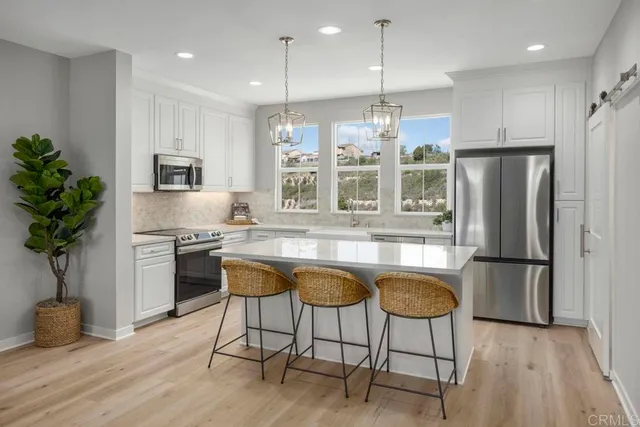 a kitchen with stainless steel appliances granite countertop a refrigerator a stove a sink dishwasher and a dining table with wooden floor