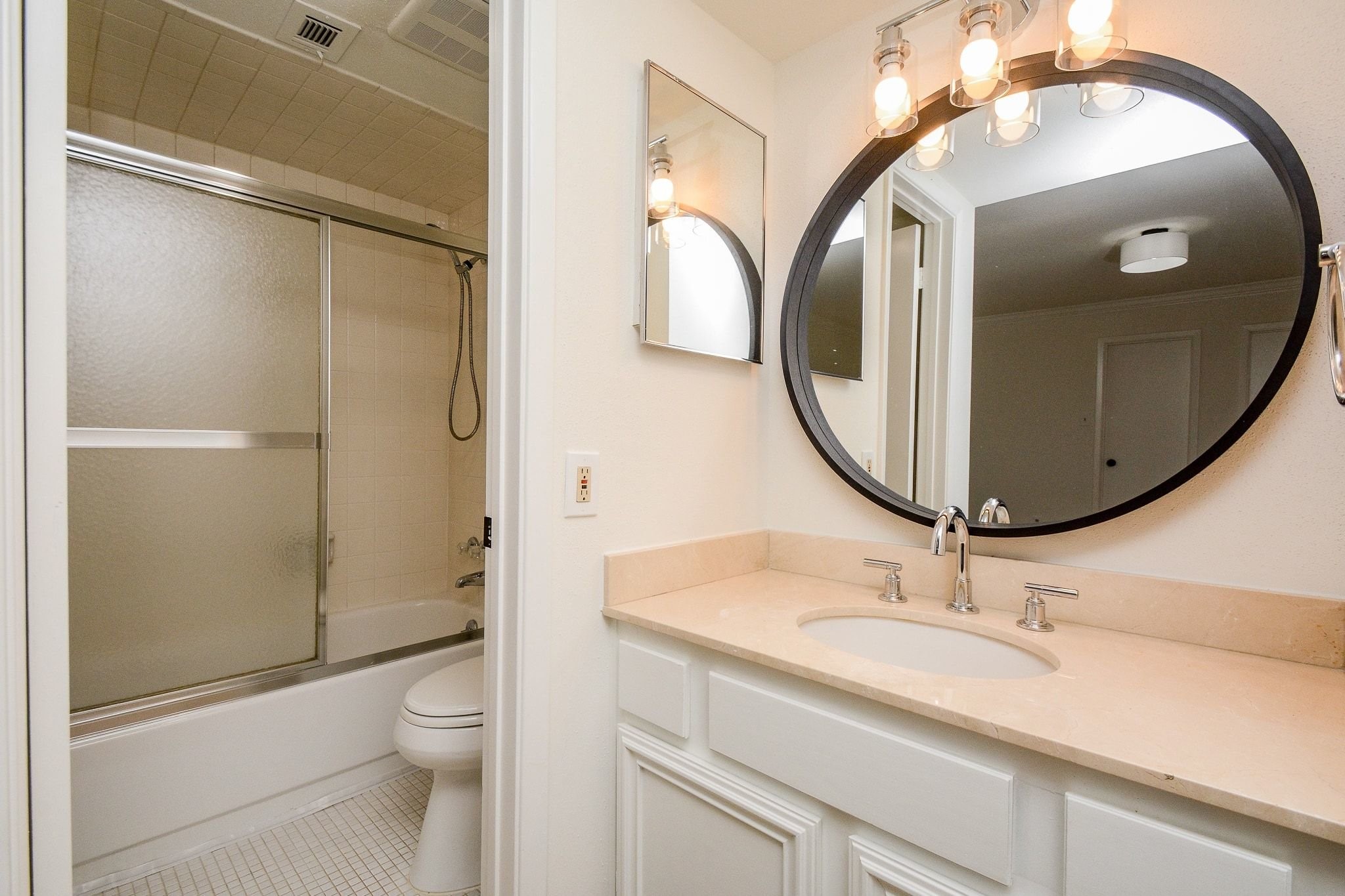 820 Harold Street Houston, TX 77006 - Photo 29 of 33 The en suite features a round black-framed mirror, updated white vanity with quartz countertop, chrome fixtures, and a tub/shower combo with glass slider doors.