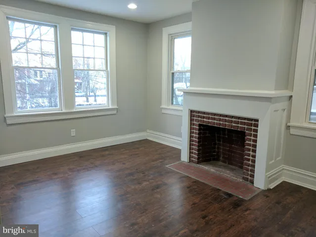 an empty room with wooden floor fireplace and windows