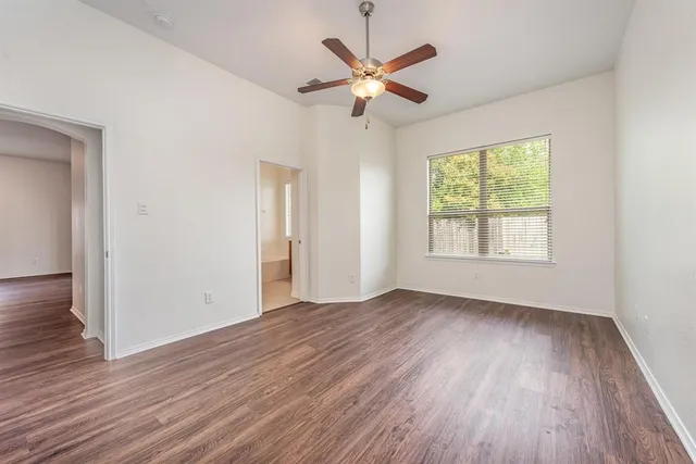 an empty room with wooden floor fan and windows