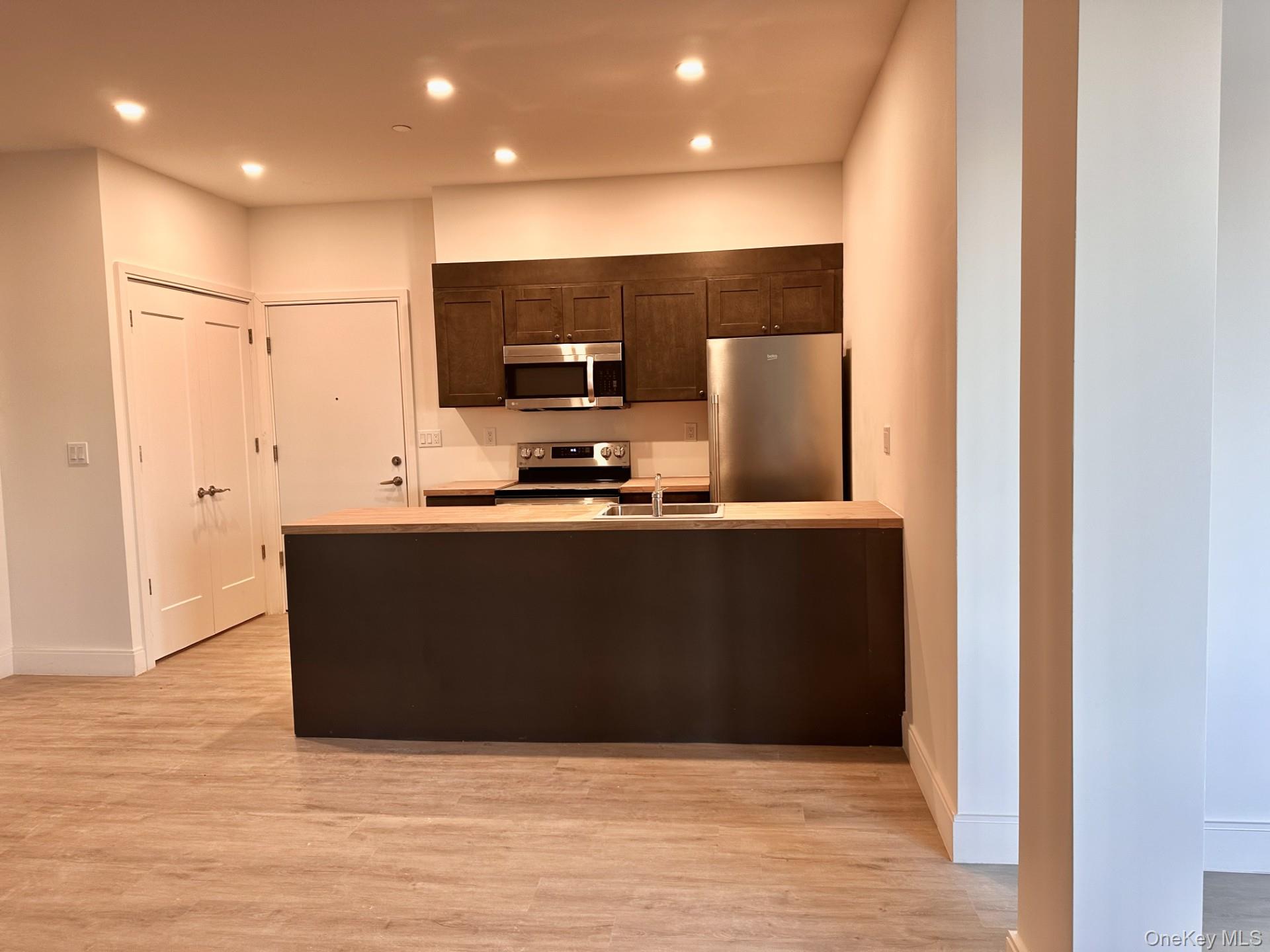Kitchen featuring appliances with stainless steel finishes, a peninsula, light countertops, dark brown cabinetry, and light wood finished floors