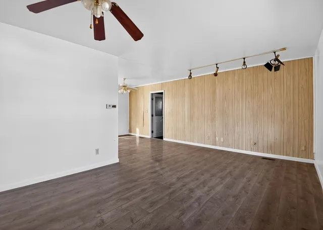 a view of an empty room with wooden floor ceiling fan
