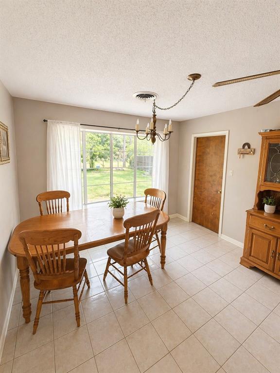504 Aspen Road Gainesville, TX 76240 - Photo 3 of 11 Spacious room featuring light-toned tile flooring, a large window with ample natural light, a wood-finish door, and a multi-light chandelier