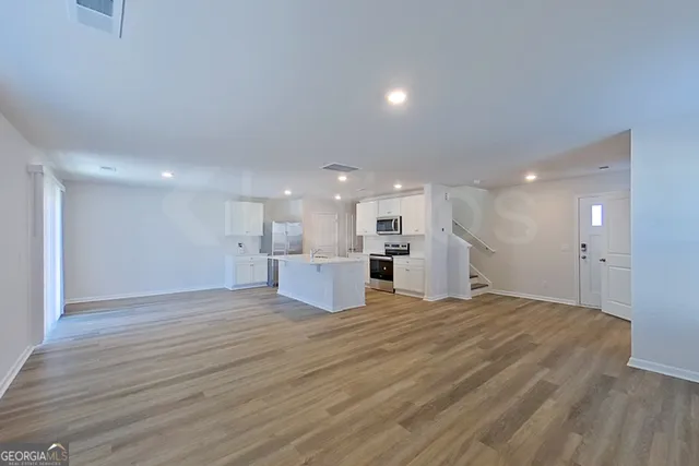 a view of an empty room with wooden floor and kitchen