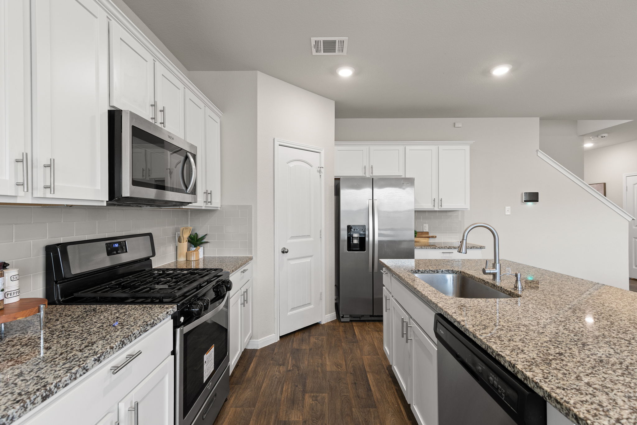 281 Jayden Drive Kyle, TX 78640 - Photo 14 of 36 Modern kitchen featuring stainless steel appliances, granite countertops, white cabinetry with brushed nickel hardware, a subway tile backsplash, and wood-finish flooring