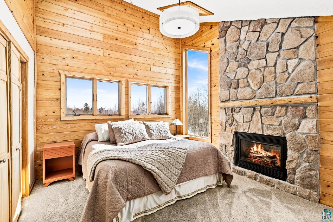 67 Snowshoe Trail Tofte, MN 55615 - Photo 7 of 42 Bedroom featuring wood walls, light carpet, a stone fireplace, and a closet