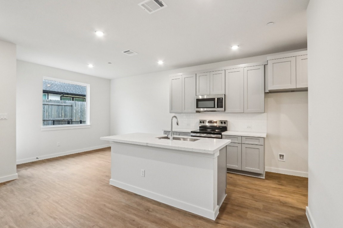 2600 Gattis School Road, Unit 1001 Round Rock, TX 78664 - Photo 9 of 36 a kitchen with stainless steel appliances granite countertop a stove a sink a refrigerator white cabinets and wooden floor next to a window