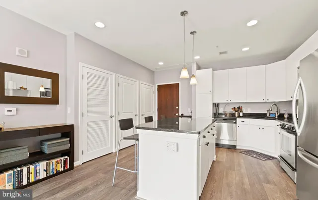 a kitchen with stainless steel appliances kitchen island granite countertop a stove a sink a refrigerator and white cabinets with wooden floor