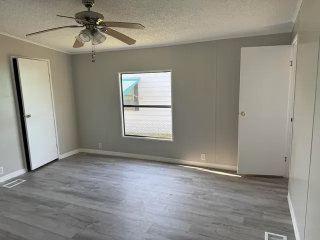 an empty room with wooden floor fan and windows