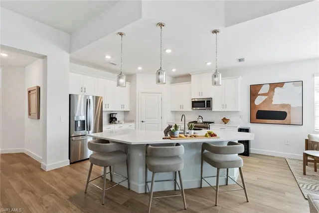 a kitchen with stainless steel appliances kitchen island granite countertop a dining table chairs and a refrigerator a sink