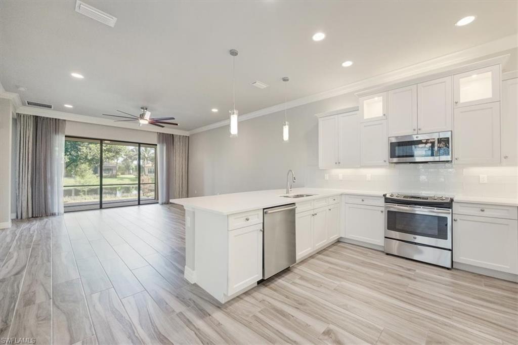 13418 Silktail Drive Naples, FL 34109 - Photo 16 of 36 a large kitchen with stainless steel appliances granite countertop a stove a sink and white cabinets with wooden floor next to windows