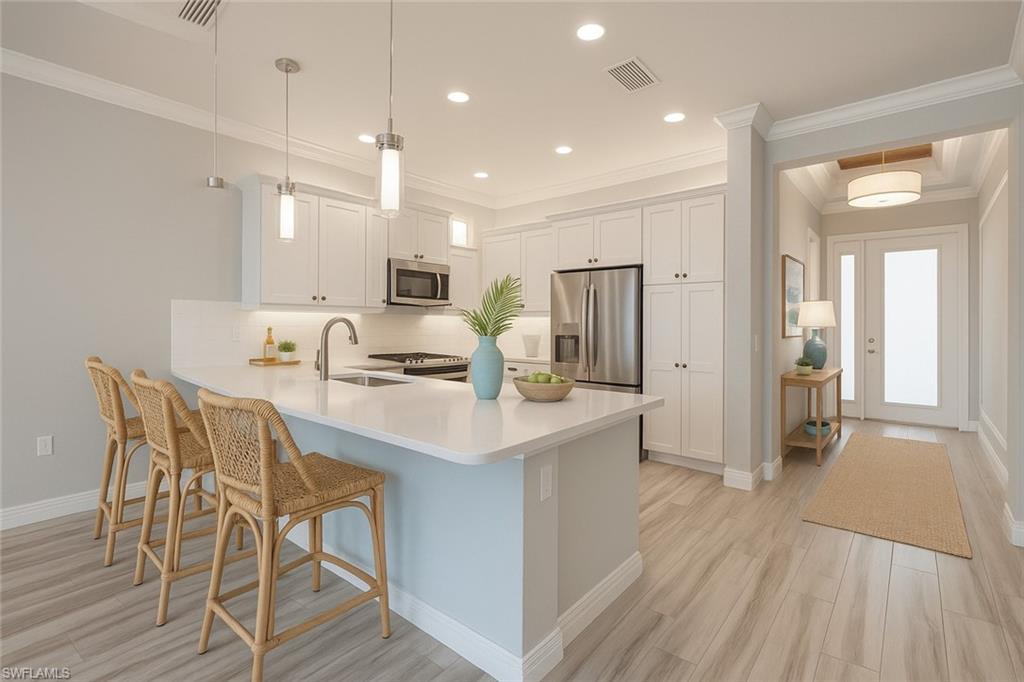13418 Silktail Drive Naples, FL 34109 - Photo 7 of 36 Kitchen featuring a kitchen bar, hanging light fixtures, a peninsula, white cabinetry, and appliances with stainless steel finishes