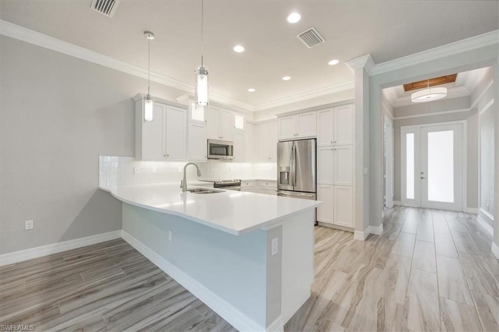 13418 Silktail Drive Naples, FL 34109 - Photo 9 of 36 a large kitchen with kitchen island a sink dishwasher a refrigerator and wooden floor
