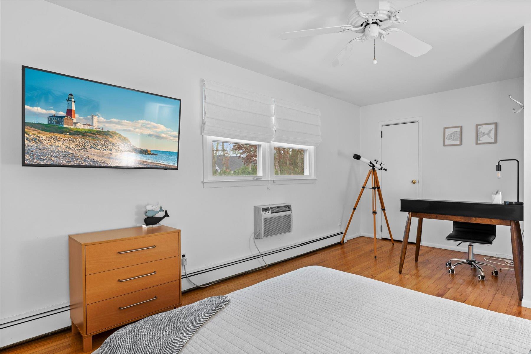 3 Crestview Drive Remsenburg, NY 11960 - Photo 9 of 21 Bedroom with baseboard heating, a baseboard radiator, an AC wall unit, a ceiling fan, and wood finished floors