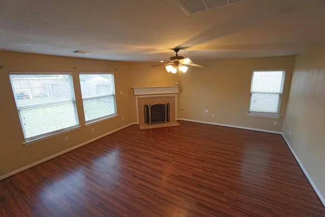 a view of an empty room with wooden floor fireplace and a window