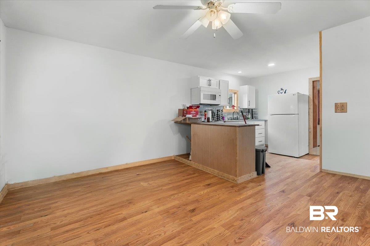 21011 River Road Robertsdale, AL 36567 - Photo 23 of 29 Open-concept common area featuring wood-finish flooring, a ceiling fan with light fixture, and an L-shaped kitchen with white cabinetry, a microwave, and a refrigerator