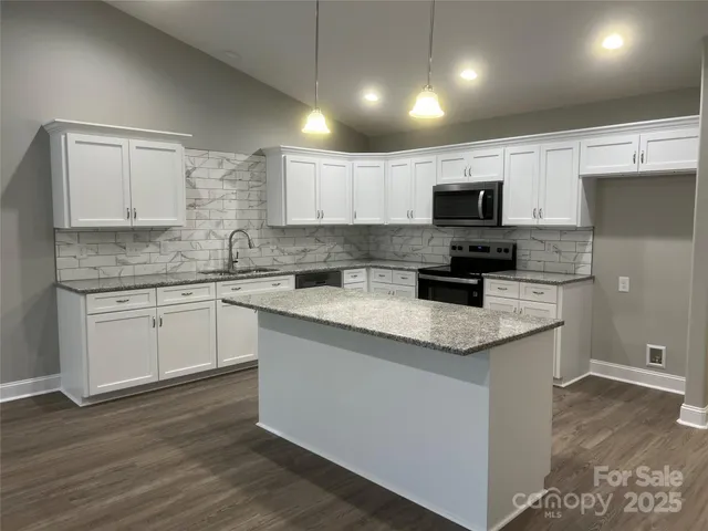 a kitchen with stainless steel appliances granite countertop a sink a stove a microwave a refrigerator a white cabinets and wooden floor