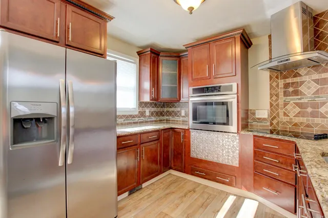 a kitchen with stainless steel appliances granite countertop a refrigerator a oven and white cabinets with wooden floors