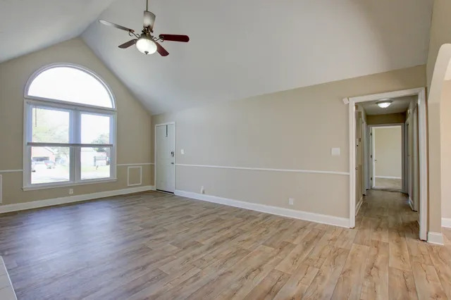 an empty room with wooden floor chandelier fan and windows