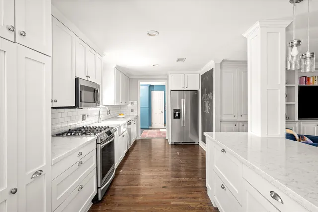 a large white kitchen with stainless steel appliances granite countertop a lot of counter space and wooden floors