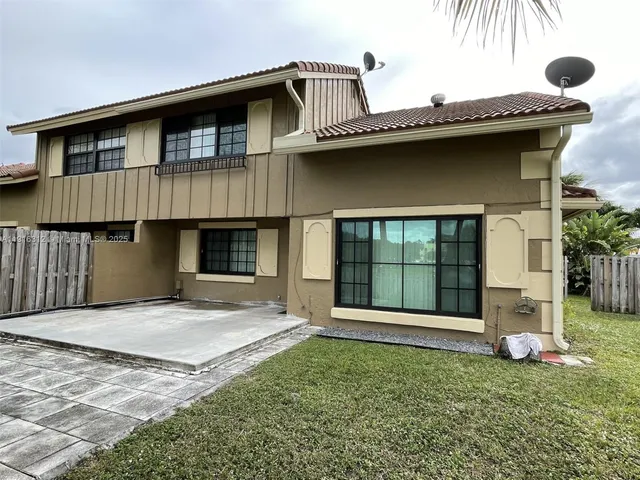 a view of yellow house with a big yard and potted plants