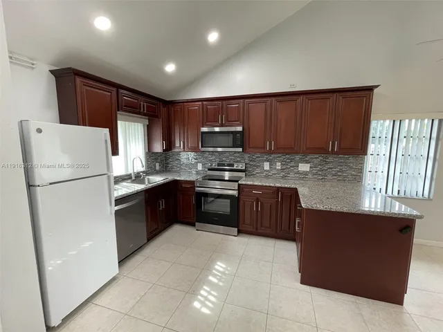 a kitchen with granite countertop a refrigerator a sink a stove a microwave and island