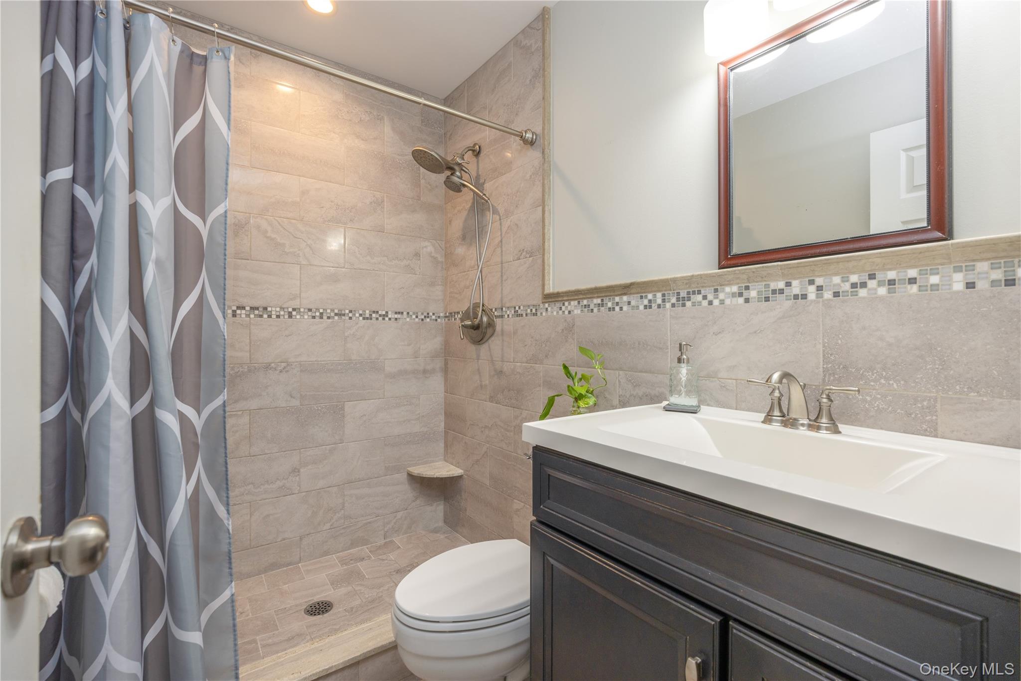 395 Ehrhardt Road Pearl River, NY 10965 - Photo 12 of 34 Modern bathroom featuring a spacious walk-in shower with tile surround and glass enclosure, a sleek vanity with white quartz countertop and dual-sink configuration, brushed nickel fixtures, and mosaic tile accent band