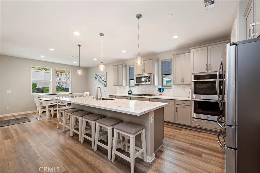 39526 Verbena Way Temecula, CA 92591 - Photo 5 of 55 a kitchen with stainless steel appliances a stove a sink dishwasher a refrigerator and white cabinets with wooden floor