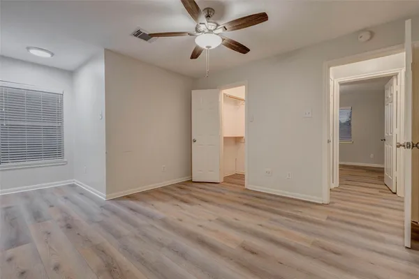 a view of an empty room with wooden floor and a ceiling fan
