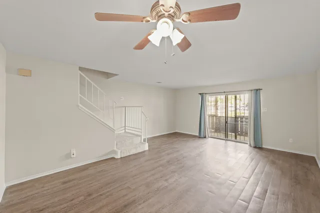 an empty room with wooden floor chandelier fan and windows