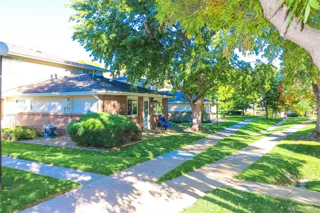 a view of a brick house with a big yard plants and large trees