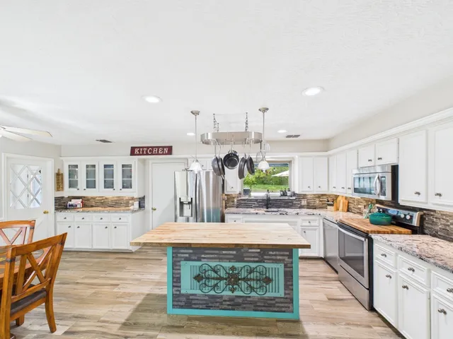 a kitchen with stainless steel appliances kitchen island granite countertop a stove a sink dishwasher and white cabinets with wooden floor