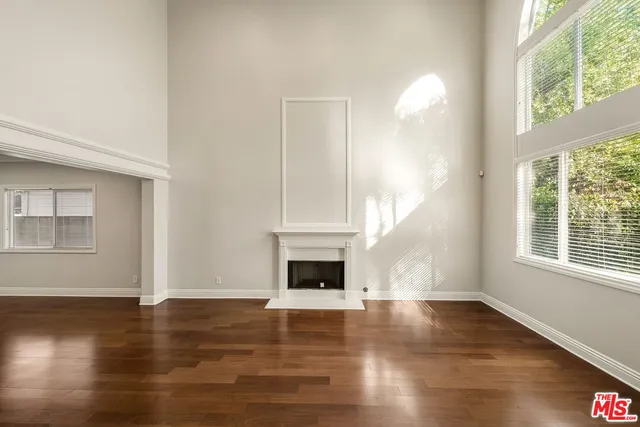 an empty room with wooden floor fire place and windows