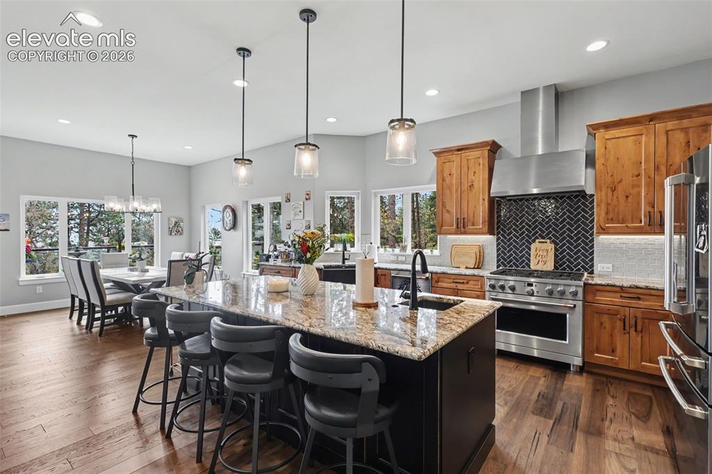 21 Leaming Road Colorado Springs, CO 80906 - Photo 21 of 48 Spacious kitchen featuring an expansive center island with seating, stainless steel appliances, herringbone tile backsplash, wood-finish flooring, and ample natural light