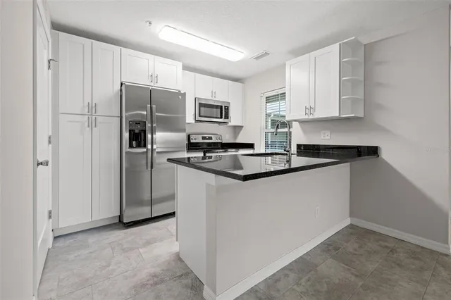 a kitchen with stainless steel appliances granite countertop a refrigerator a stove a sink and white cabinets
