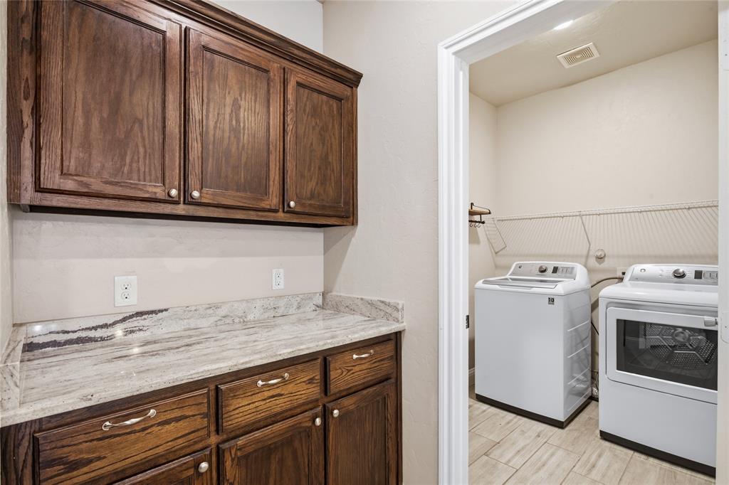 1502 Reed Street Greenville, TX 75401 - Photo 12 of 26 Laundry room featuring wood-finish cabinetry, light-toned countertops, and tiled flooring