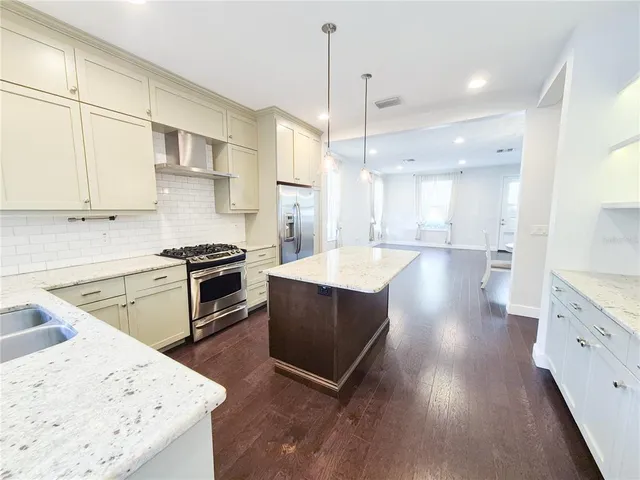 a kitchen with stainless steel appliances kitchen island granite countertop a sink a stove and a wooden floors