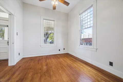 an empty room with wooden floor chandelier fan and windows