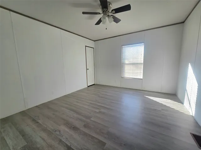 an empty room with wooden floor fan and windows