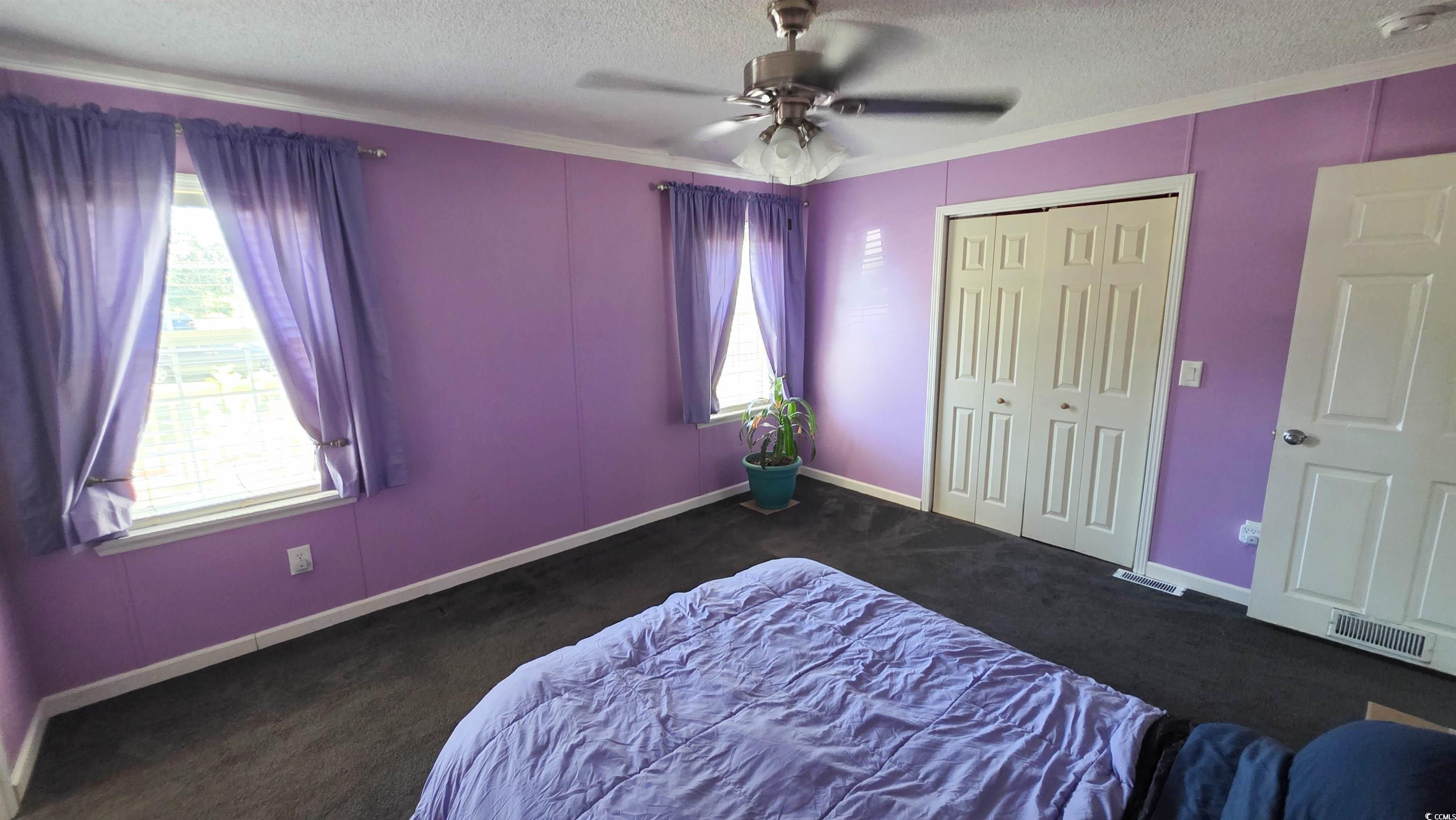 2018 Venus Court Loris, SC 29569 - Photo 13 of 17 Bedroom featuring a textured ceiling, dark carpet, multiple windows, ornamental molding, and a ceiling fan