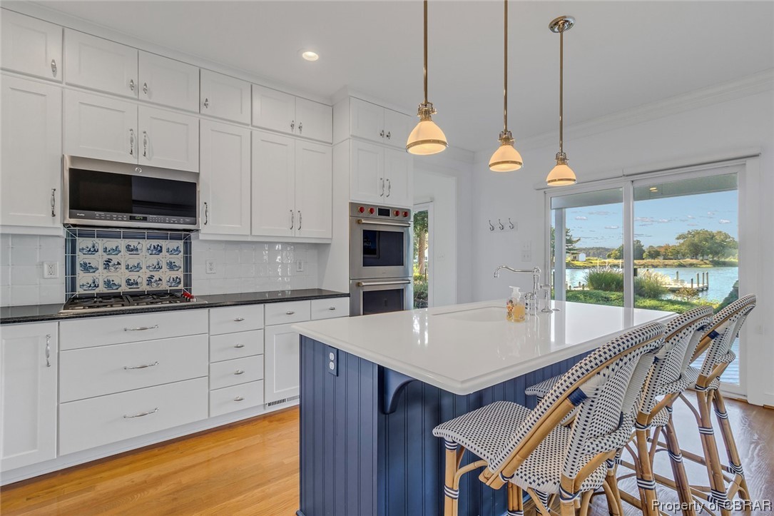 192 Bayberry Point Lane Kilmarnock, VA 22482 - Photo 24 of 49 Kitchen featuring backsplash, light hardwood floors, white cabinetry, a center island, crown molding, pendant lighting, and stainless steel appliances