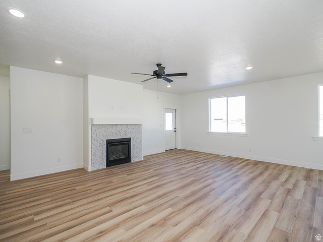 3938 North Wood Road Eagle Mountain, UT 84005 - Photo 9 of 55 Unfurnished living room with light wood-style floors, ceiling fan, a tiled fireplace, and recessed lighting