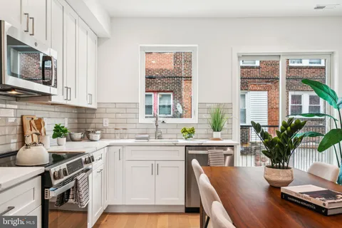 a kitchen with stainless steel appliances a white table chairs refrigerator and microwave