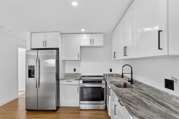 a kitchen with stainless steel appliances granite countertop a refrigerator a sink a stove and white cabinets with wooden floor