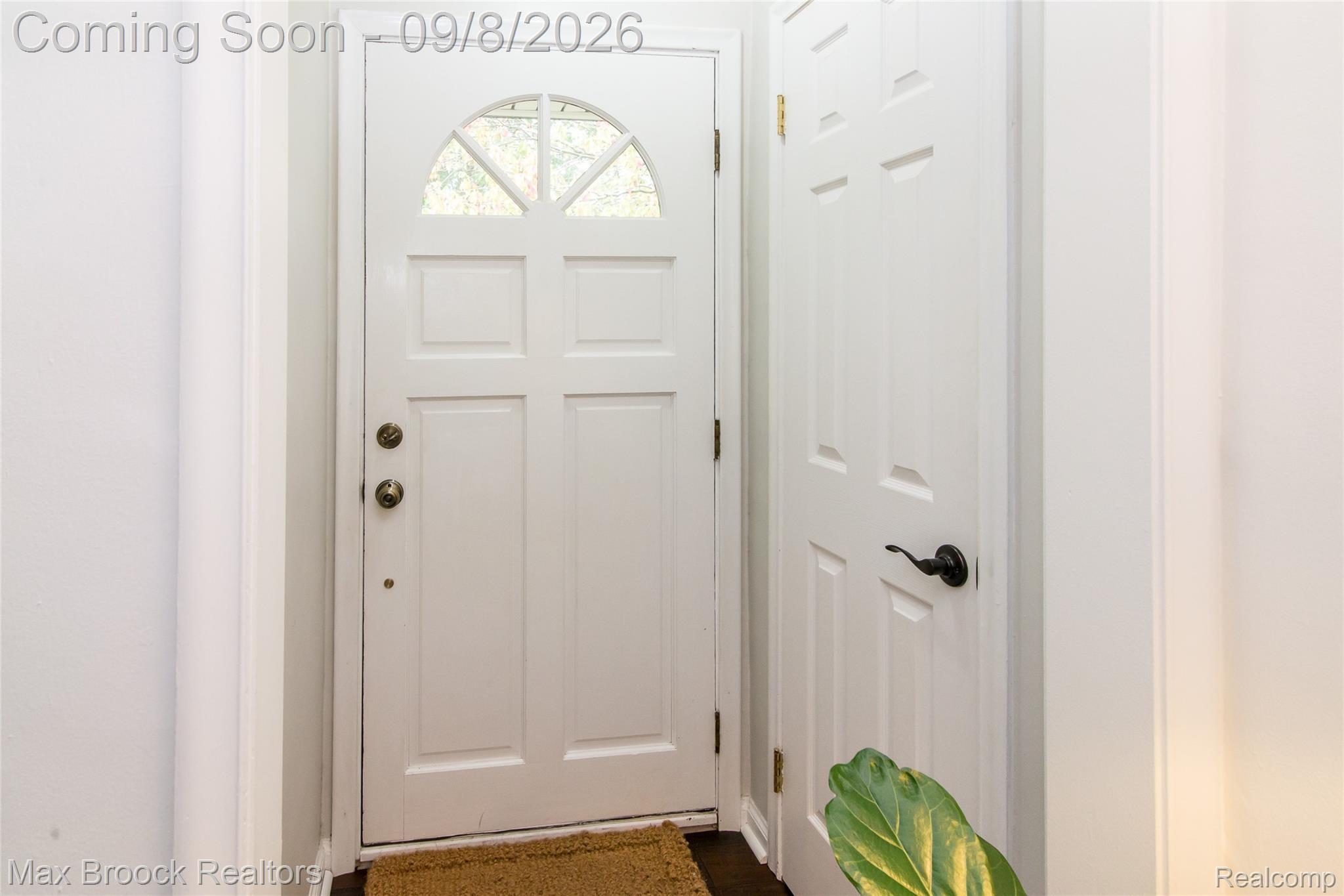 White paneled front door with an arched transom window and brass hardware